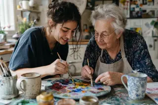 Two people of different ages mixing paint together at a messy kitchen table, hands close, in a softly lit, warm and creative domestic space.