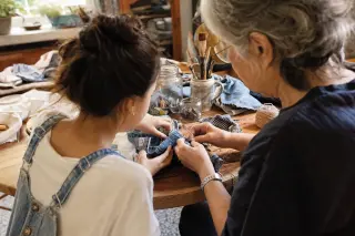 Two people of different generations collaborating at a kitchen table, creatively reusing upcycled materials in natural daylight, hands busy with a handmade project in a cozy, lived-in space.